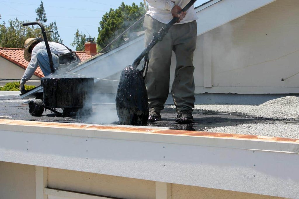 Workers use Hot Mop to lay down molten tar asphalt sheets and pea gravel on a flat roof Hot Mop Roof Repair https://www.capitolroofingcompany.com/hot-mop-roof-repair/